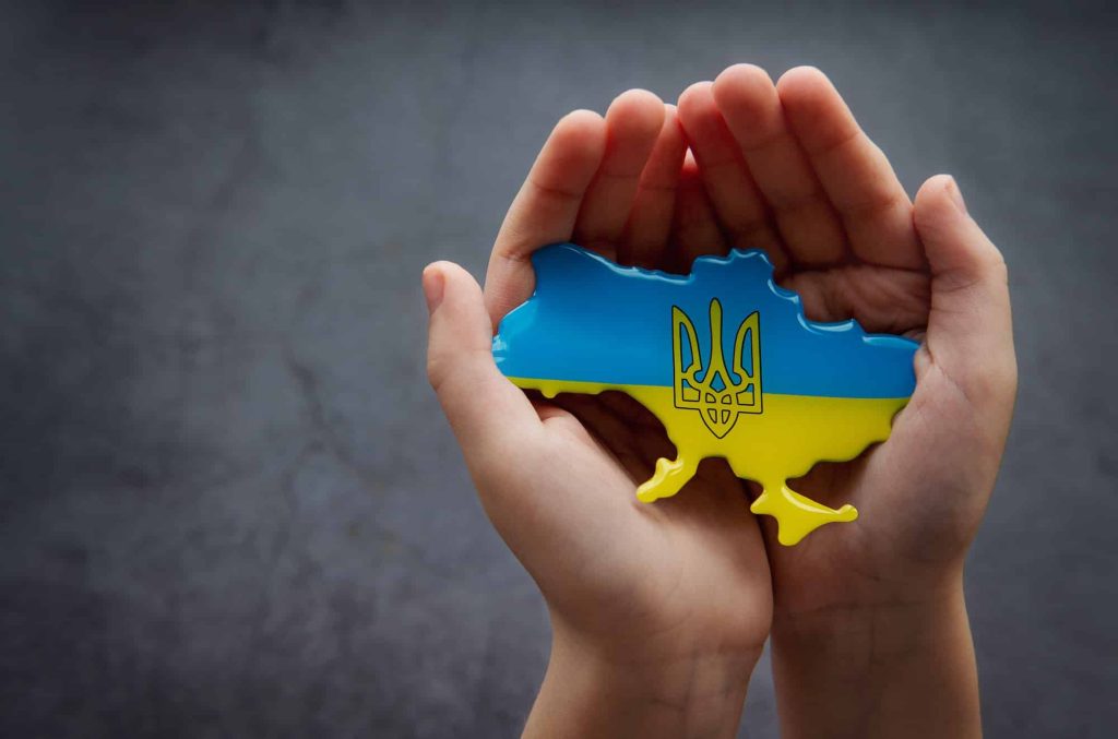 Hands holding the shape of Ukraine border with color flag. Stand with Ukraine